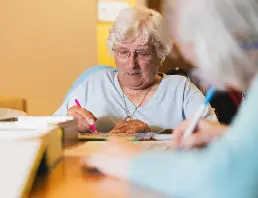 Elderly woman writing at table in High Brake House care home, Clitheroe, Lancashire