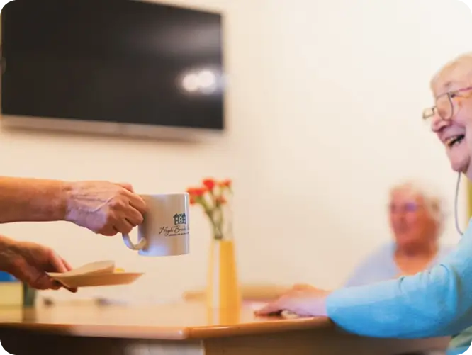 Smiling resident enjoying coffee with others in a warm Clitheroe care home