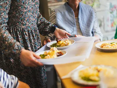 Person in floral dress serving food on tray to residents at High Brake House, Clitheroe