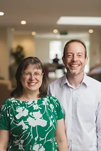 Two people smiling indoors at Clitheroe care home, green floral dress and light shirt